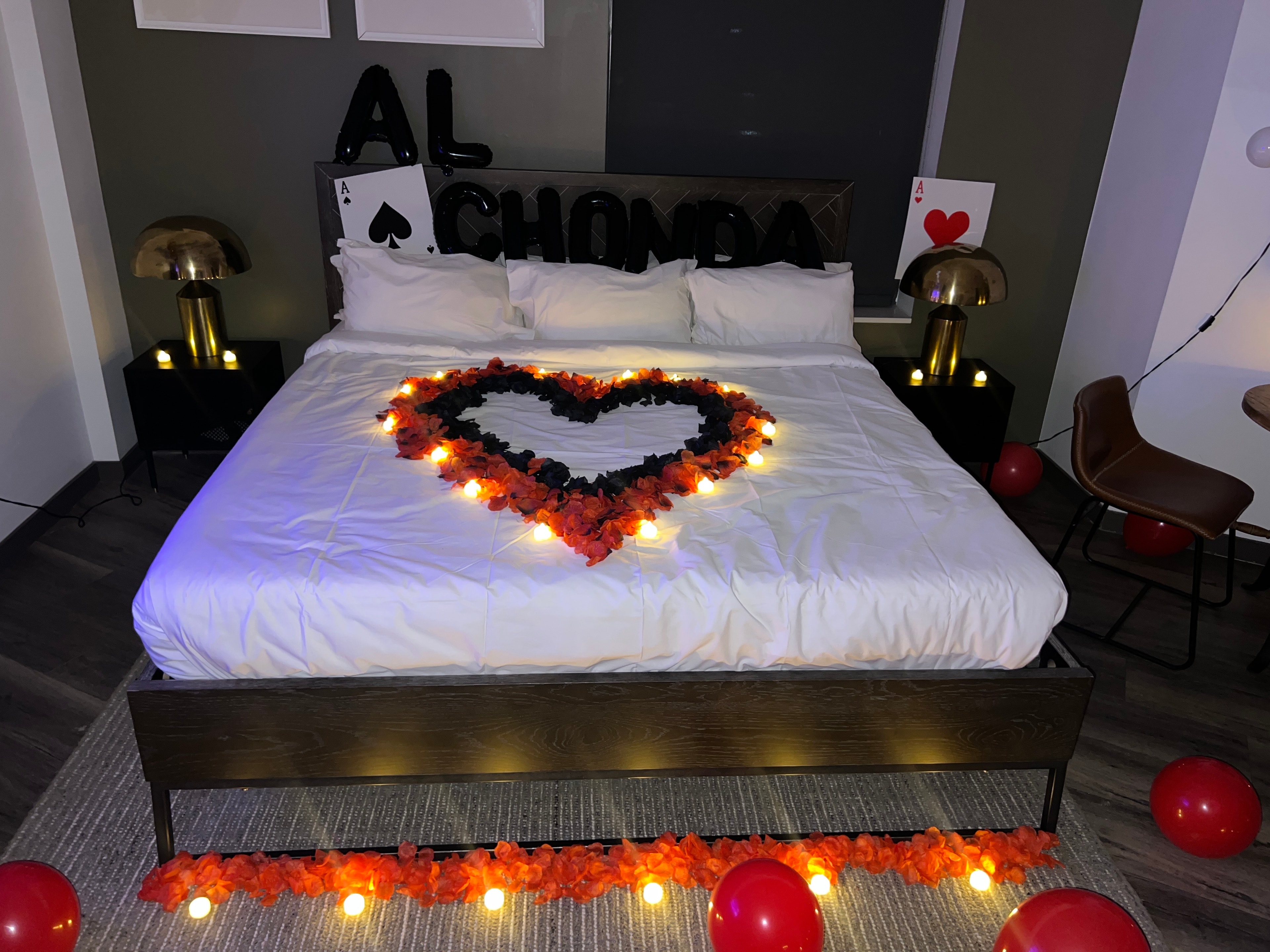 Romantic hotel room with rose petal heart on bed and personalized balloons